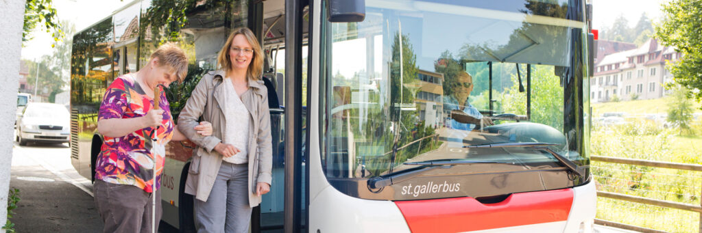 Blinde Frau die von Begleitperson aus dem Bus geführt wird.