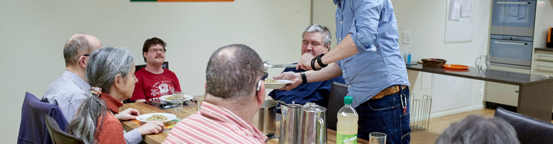 Bewohnerinnen und Bewohner mit Betreuer beim Mittagessen